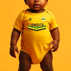 Puede incluir: Un body de bebé amarillo con mangas cortas. El body presenta la palabra "JAMAICA" en verde y negro, con el número "10" y una pequeña bandera jamaicana. El bebé está de pie frente a un fondo naranja.