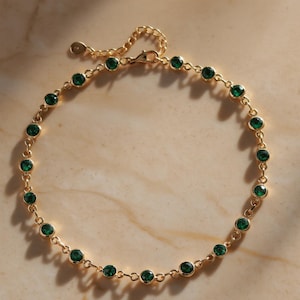 Peut inclure: Un bracelet de cheville en chaîne dorée orné de pierres précieuses rondes vert émeraude. Le bracelet de cheville a un design délicat avec une fermeture à fermoir. Les pierres précieuses sont espacées uniformément le long de la chaîne.