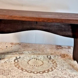 May include: A dark brown wooden bench with a rectangular top and curved legs. The bench is made of solid wood and has a simple, rustic design. The bench is approximately 91 cm long.