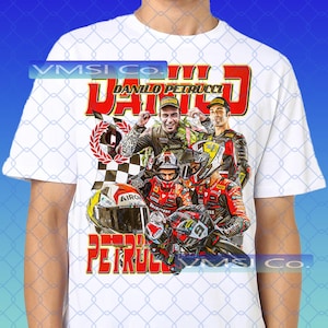 Puede incluir: Camiseta blanca con un gráfico colorido de Danilo Petrucci, piloto de motos. El diseño incluye su nombre en rojo, imágenes de él, una bandera a cuadros y una motocicleta. La camiseta tiene cuello redondo y mangas cortas.
