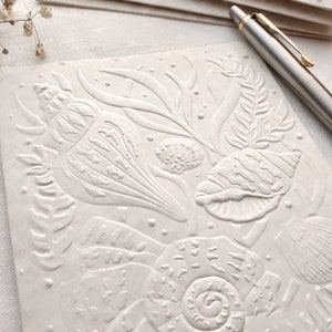 May include: White embossed paper with a design of seashells and seaweed. The paper has a textured, raised surface.