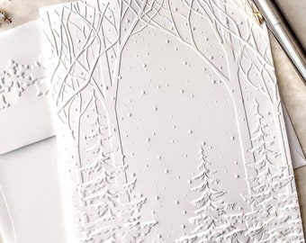 May include: A white embossed card with a winter scene of trees and falling snow. The card is blank inside for writing a message.