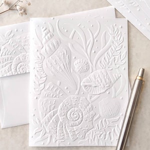 May include: White embossed card with a design of seashells and seaweed. The card is blank and can be used for a variety of occasions.