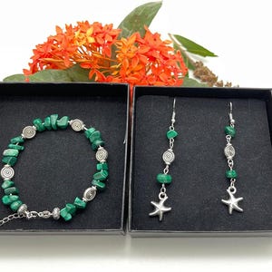 May include: A jewelry set featuring a bracelet and earrings, presented in black boxes. The bracelet and earrings are adorned with green malachite stones and silver-toned spiral and starfish charms. The set is displayed against a backdrop of orange flowers.