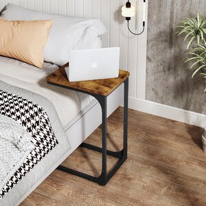 May include: A small, brown and black side table with a laptop on top. The table has a rectangular, wood-look surface and a black metal frame. The table is 24 inches high, 16 inches wide, and 12 inches deep.