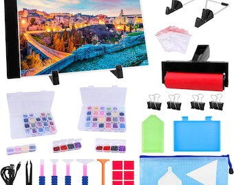 May include: A diamond painting kit featuring a light board with a landscape image, various containers of colorful gems, tools, a roller, and other accessories. The kit includes a blue zippered pouch and a stand for the light board.