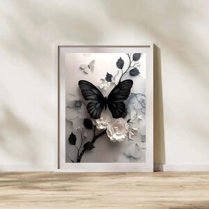 Op de afbeelding: Een ingelijst kunstwerk met een zwarte vlinder met gedetailleerde vleugels, zittend op witte papieren bloemen en takken. Het kunstwerk heeft een 3D-effect, met een zachte, neutrale achtergrond. De lijst is wit en het kunstwerk wordt op een houten oppervlak tentoongesteld.
