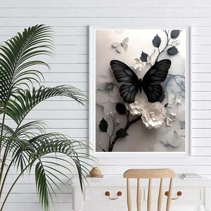 Op de afbeelding: Een ingelijst kunstwerk met een zwarte vlinder met gedetailleerde vleugelpatronen, tegen een achtergrond van witte bloemen en grijs blad. Het kunstwerk zit in een witte lijst, wat een opvallend contrast cre&euml;ert.