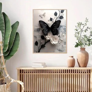 Op de afbeelding: Een ingelijst kunstwerk met een zwarte vlinder met gedetailleerde vleugels, tegen een achtergrond van witte en grijze bloemelementen. Het kunstwerk zit in een lichte houten lijst, wat een moderne en elegante uitstraling cre&euml;ert.