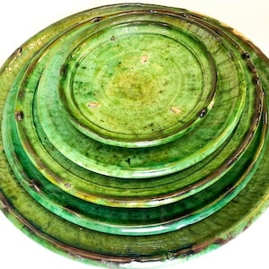 以下が含まれることがあります： さまざまなサイズの6つの緑色のセラミックプレートのスタック。プレートは光沢仕上げで、縁に濃い緑色と茶色のアクセントが付いています。プレートは入れ子状に配置されており、一番下のプレートが一番大きいです。