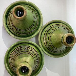 Op de afbeelding: Drie groene keramische tajinepotten met conische deksels. Elke pot heeft een cirkelvormige basis en een deksel met een centrale knop en decoratieve bruine geëtste patronen. De tajines zijn gerangschikt op een wit oppervlak.