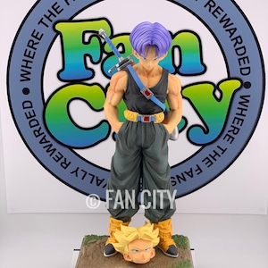 Può includere: Statuetta dettagliata di un personaggio con i capelli viola, che indossa una canotta nera e pantaloni verdi, con una spada sulla schiena. La statuetta è su una base con una testa staccata. La base ha il testo "TORANKUSU" e il logo Fan City.