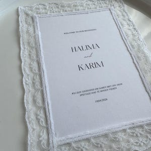 Op de afbeelding: Een witte uitnodigingskaart met een delicate kanten rand, met de namen "HALIMA and KARIM" en de tekst "WELCOME TO OUR BEGINNING". De datum "19/04/2026" is ook zichtbaar.