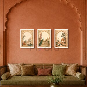 May include: Three rectangular wall art prints featuring detailed illustrations of Mughal-style architecture, lush gardens, and peacocks. Each print is framed in a white border and displays intricate floral motifs and arched gateways in warm tones.