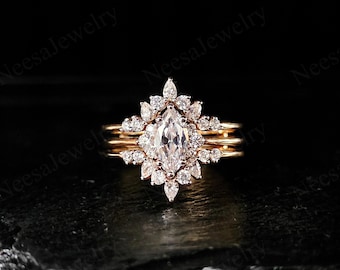 May include: A marquise-cut diamond engagement ring with a halo of smaller diamonds, set on a gold band. The ring is part of a three-piece set, with two additional gold bands. The jewelry is displayed against a dark background.