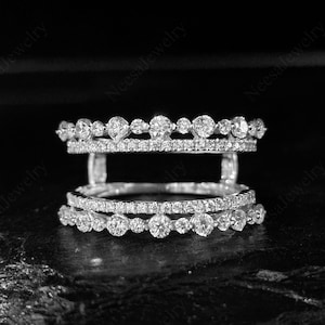 Op de afbeelding: Een drielaagse diamanten ring met een uniek open ontwerp. De ring heeft meerdere rijen kleine, sprankelende diamanten, met grotere stenen in een decoratief patroon op de bovenste en onderste niveaus.