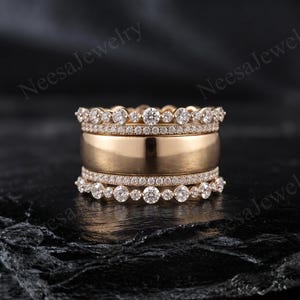 May include: A stack of three gold rings featuring a wide, smooth central band flanked by two thinner bands. Each outer band is adorned with a row of small, round, clear stones and a scalloped edge of larger, round, clear stones. Text reads NeesaJewelry.