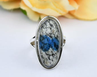 May include: A silver ring featuring an oval-shaped stone with a speckled white and gray pattern and a vibrant blue center. The ring has a polished finish and a simple band design, suitable for everyday wear.