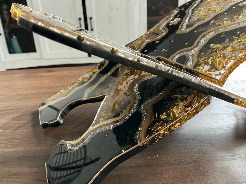 May include: A decorative, handcrafted stand with a black, gold, and silver resin design. The stand features a layered effect with gold leaf accents and a glossy finish. The edges are outlined in gold, creating a luxurious aesthetic.