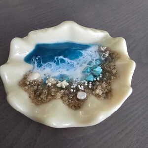 May include: An off-white seashell-shaped dish with a miniature beach scene. The scene features a blue ocean, sand, turquoise stones, tiny shells, and miniature sea creatures. The dish is a unique, handcrafted item.