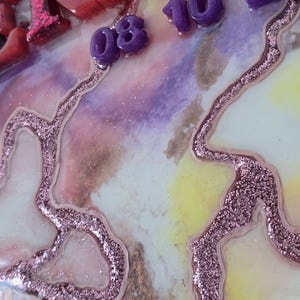 Puede incluir: Primer plano de una pieza de arte decorativa de resina con un fondo marmolado colorido. La pieza presenta letras y n&uacute;meros en relieve y brillantes en tonos de rojo, rosa y morado. Los n&uacute;meros indican "08 10 20".