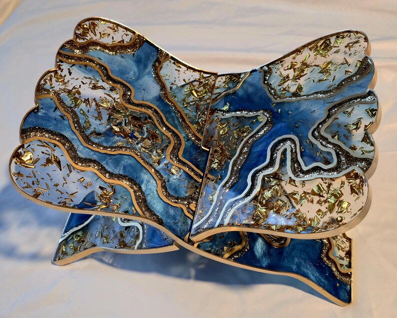 May include: A decorative wooden book stand with a unique design. The stand features a blue and white resin design with gold leaf accents. The edges are trimmed with gold and brown. The stand is designed to hold a book open.