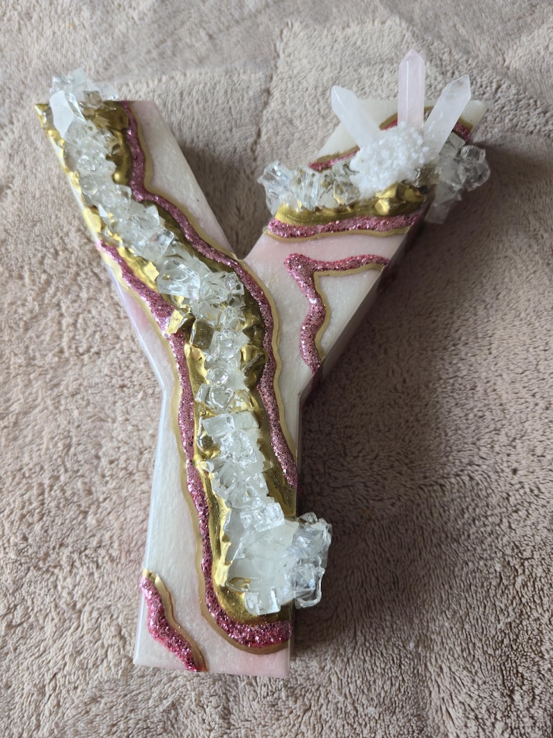 May include: A decorative letter "Y" in a geode style. The letter is white with pink glitter accents and gold trim. Clear crystals and quartz clusters are embedded throughout the design, creating a unique, eye-catching piece.