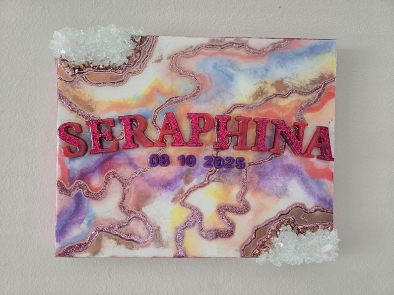 Puede incluir: Un lienzo rectangular con un dise&ntilde;o abstracto colorido en tonos rosa, morado, amarillo y azul. El nombre "SERAPHINA" se muestra en letras rosas brillantes, con la fecha "08 10 2025" debajo. Adornos cristalinos transparentes adornan los bordes.
