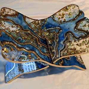 May include: A decorative wooden book stand with a unique design. The stand features a blue and white marbled pattern with gold leaf accents. The edges are outlined in gold. The stand is designed to hold a book open.
