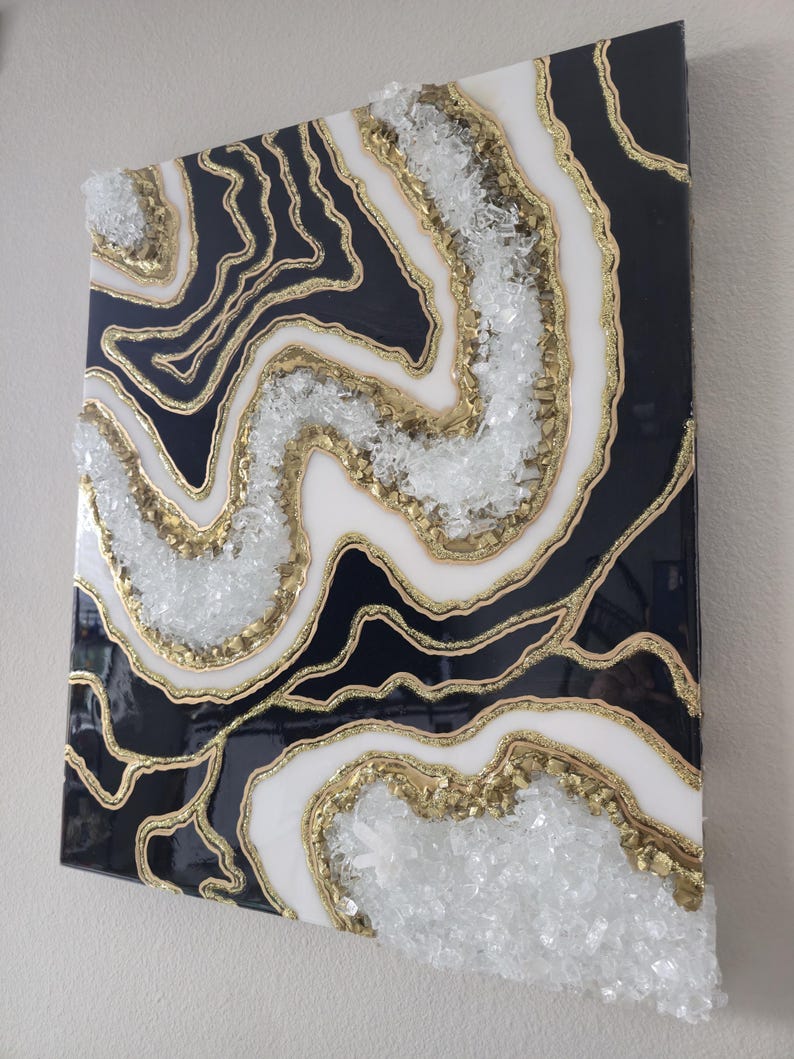 May include: Abstract wall art with a geode design. The artwork features a black, white, and gold colour scheme, with clear crystal accents. The design resembles natural stone formations, creating a unique decorative piece.