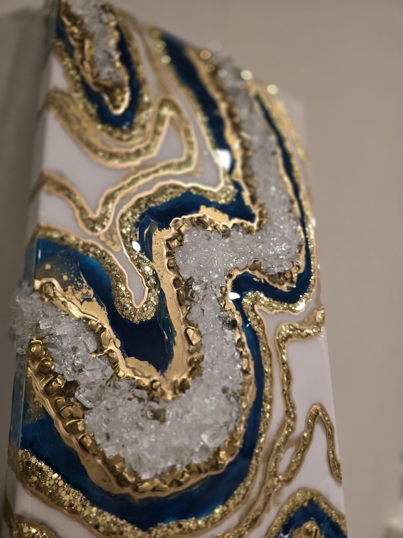 May include: Abstract art piece with a geode design. The artwork features a white base with blue and gold accents, and clear crystal-like embellishments. The piece has a rectangular shape.