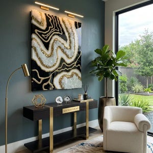May include: A striking piece of abstract wall art in black, white, and gold adorns a dark wood console table with gold supports. A cream armchair and patterned rug complete the modern interior. The console bears the text "LUXE SIGNATURE ART".