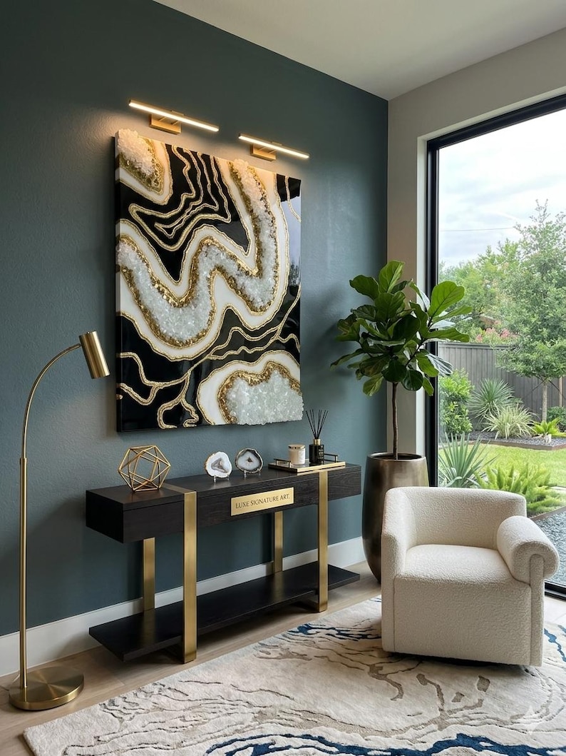 May include: A striking piece of abstract wall art in black, white, and gold adorns a dark wood console table with gold supports. A cream armchair and patterned rug complete the modern interior. The console bears the text "LUXE SIGNATURE ART".