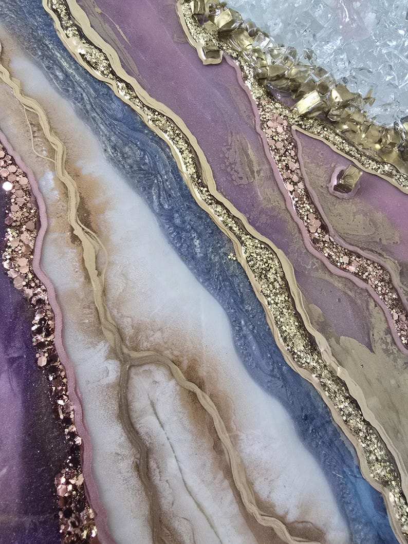 Może przedstawiać: Abstrakcyjne dzieło sztuki o płynnym wzorze. Zawiera odcienie fioletu, niebieskiego, białego i złota. Złoty brokat i teksturowane złote akcenty tworzą efekt warstwowy. Unikalna, organiczna estetyka.