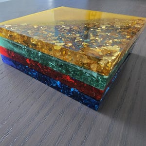 Pode incluir: Uma pilha de blocos de resina coloridos. O bloco superior &eacute; amarelo com inclus&otilde;es de folhas de ouro. Abaixo est&atilde;o blocos verdes, vermelhos e azuis. Os blocos s&atilde;o empilhados, criando uma apar&ecirc;ncia vibrante e texturizada.