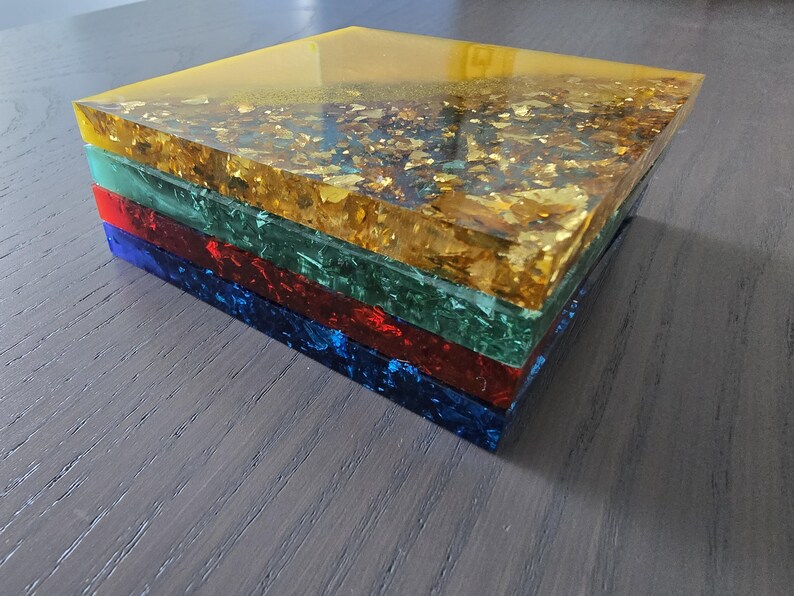 Pode incluir: Uma pilha de blocos de resina coloridos. O bloco superior &eacute; amarelo com inclus&otilde;es de folhas de ouro. Abaixo est&atilde;o blocos verdes, vermelhos e azuis. Os blocos s&atilde;o empilhados, criando uma apar&ecirc;ncia vibrante e texturizada.