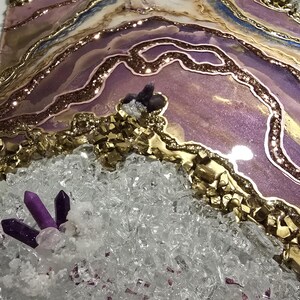 Op de afbeelding: Een abstract kunstwerk met een gelaagd ontwerp in tinten paars, goud en wit. Het stuk bevat glitter, kristallen en een geode-achtig uiterlijk. Het kunstwerk heeft een textuur met een sprankelende afwerking.