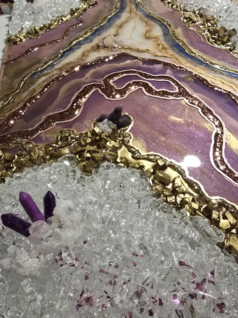 Op de afbeelding: Een abstract kunstwerk met een gelaagd ontwerp in tinten paars, goud en wit. Het stuk bevat glitter, kristallen en een geode-achtig uiterlijk. Het kunstwerk heeft een textuur met een sprankelende afwerking.