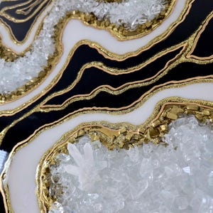 May include: Abstract geode-style artwork. The piece combines black and white sections with gold glitter and crystal embellishments. The design has a layered effect, creating a textured appearance.