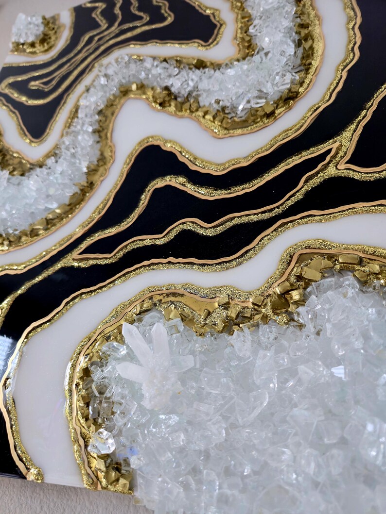 May include: Abstract geode-style artwork. The piece combines black and white sections with gold glitter and crystal embellishments. The design has a layered effect, creating a textured appearance.