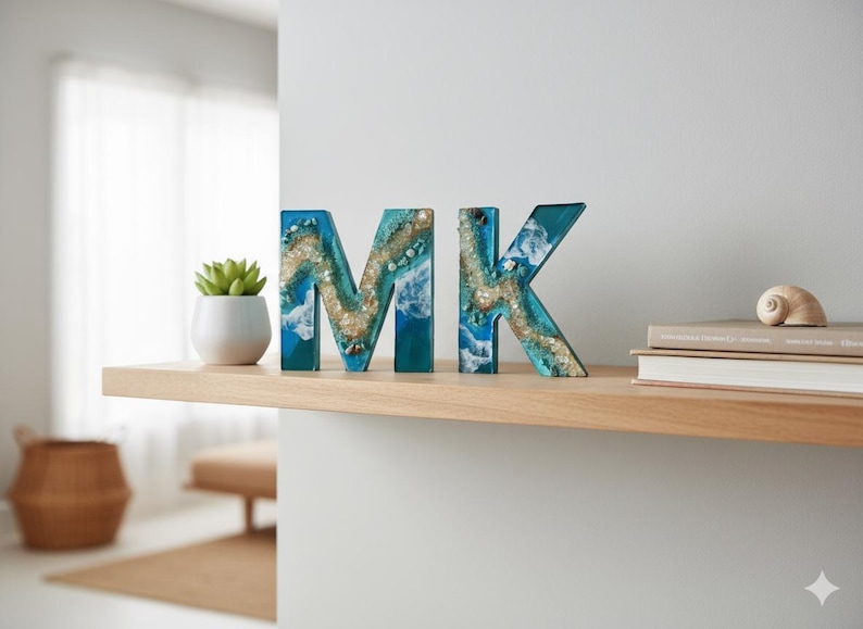 Może przedstawiać: Dekoracyjne drewniane litery piszące "MK" z motywem nadmorskim. Litery są turkusowe i niebieskie z białymi akcentami, przypominającymi fale oceanu i piasek. Litery są wyświetlane na drewnianej p&oacute;łce.