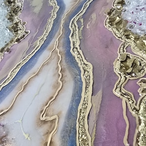 Może przedstawiać: Zbliżenie abstrakcyjnego dzieła sztuki z żywicy. Projekt łączy odcienie lawendy, bieli i błękitu, ze złotym brokatem i złotymi akcentami. Dzieło ma wygląd geody, z płynnymi liniami i teksturowanymi elementami.