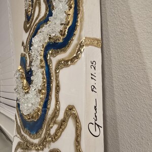 Op de afbeelding: Abstracte wandkunst met een geode-ontwerp, met blauwe, gouden en witte accenten. Het kunstwerk bevat heldere kristallen versieringen en de handgeschreven tekst "Gina 19.11.25".