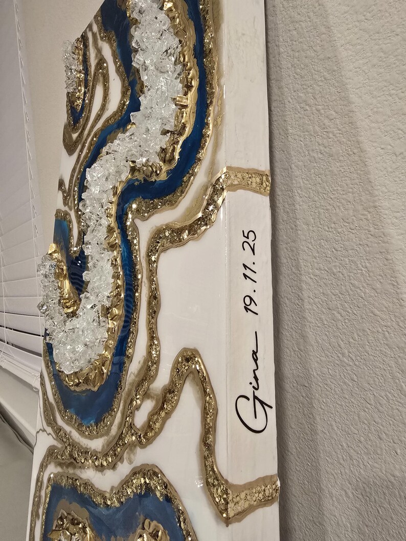 Op de afbeelding: Abstracte wandkunst met een geode-ontwerp, met blauwe, gouden en witte accenten. Het kunstwerk bevat heldere kristallen versieringen en de handgeschreven tekst "Gina 19.11.25".
