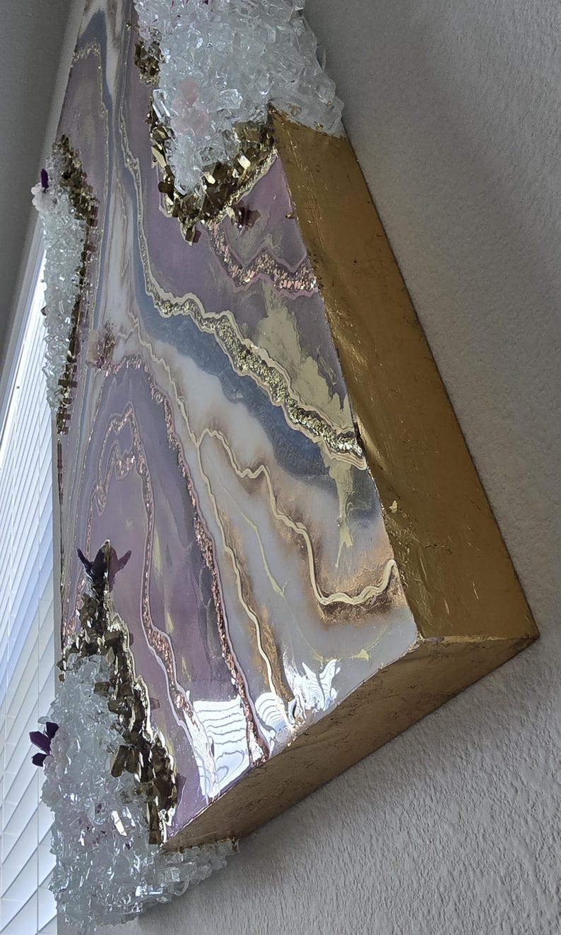 Może przedstawiać: Abstrakcyjna grafika ścienna z warstwowym wzorem w odcieniach lawendy, bieli i złota. Grafika ma żywiczne wykończenie z osadzonymi kryształami i złotymi krawędziami, tworząc efekt tekstury i wymiaru.