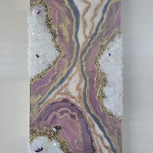 Może przedstawiać: Abstrakcyjna grafika ścienna w stylu geody, w odcieniach fioletu, złota i bieli. Grafika ma teksturowaną powierzchnię z kryształowymi zdobieniami. Prostokątny element jest zamontowany na białej ścianie. Projekt zawiera złote linie.