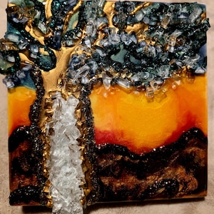 K&ouml;nnte beinhalten: Quadratisches Kunstwerk aus Kunstharz, das einen stilisierten Baum vor einem Sonnenuntergang darstellt. Der Baumstamm ist goldfarben, mit klaren Glasscherben, die die Bl&auml;tter bilden. Der Hintergrund geht von Gelb zu Rot &uuml;ber, mit dunkelbraunen und goldenen Akzenten.