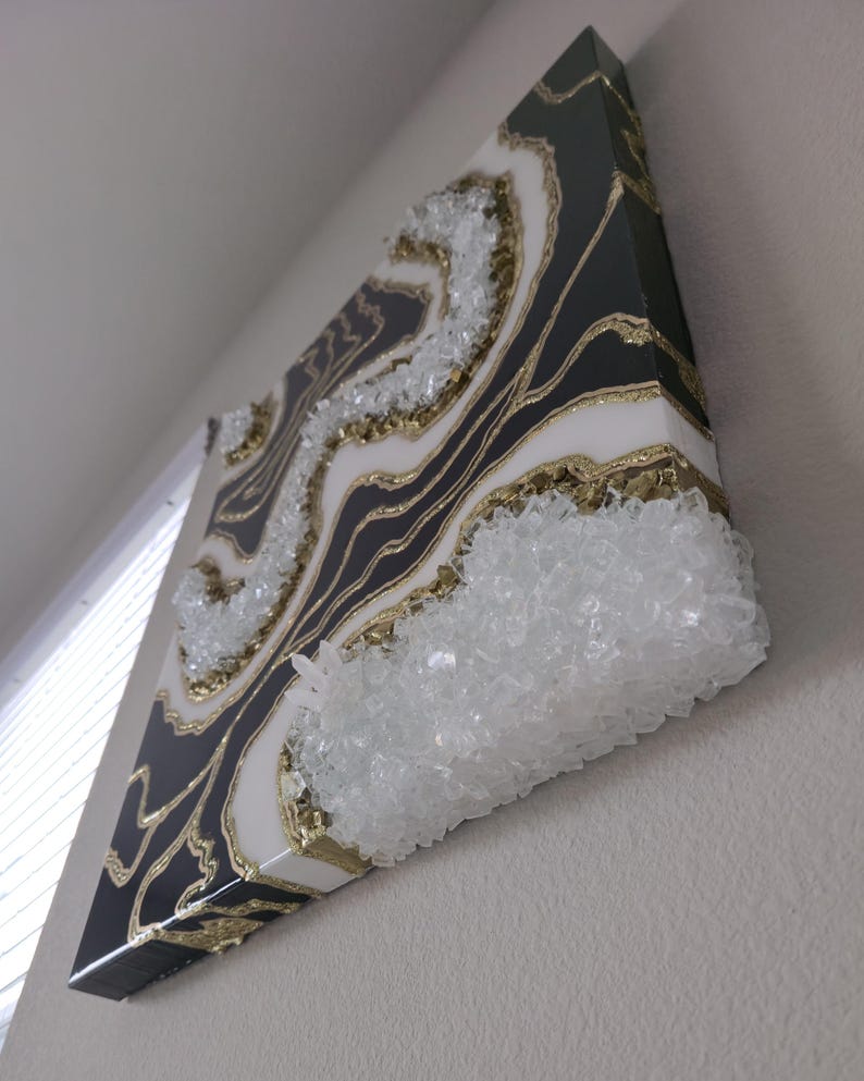 May include: Abstract wall art with a geode design. The artwork features a black and white marbled pattern with gold accents and clear crystal embellishments. The piece is mounted on a square canvas.