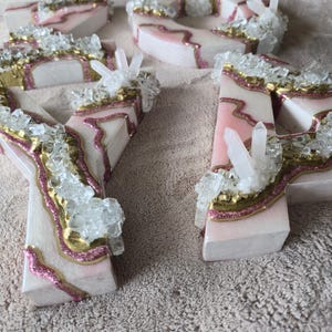 May include: Wooden letters with a pink and gold design, accented with clear crystal clusters. The letters are white with pink and gold accents, and the crystals add a sparkling touch. These decorative letters are perfect for home decor or special events.