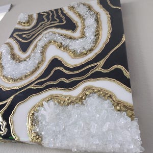 May include: Abstract wall art with a geode design. The artwork features black, white, and gold colours, with clear crystal accents. The design resembles natural stone formations.